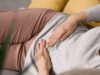 Eine Frau liegt mit Bauchschmerzen auf dem Sofa.