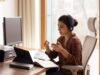 Eine Frau sitzt an einem Schreibtisch mit mehreren Bildschirmen und hat ein Headset auf. Sie kommuniziert mit ihrem Gegenüber.