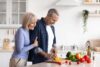 Ein älterer Mann und eine ältere Frau sind in der Küche und kochen gemeinsam.