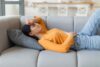 Eine junge Frau liegt auf dem Sofa und hat Bauchschmerzen.
