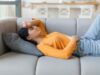 Eine junge Frau liegt auf dem Sofa und hat Bauchschmerzen.